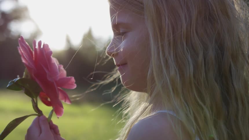 A little girl stands in a field smiling at the large pink flower in her hand