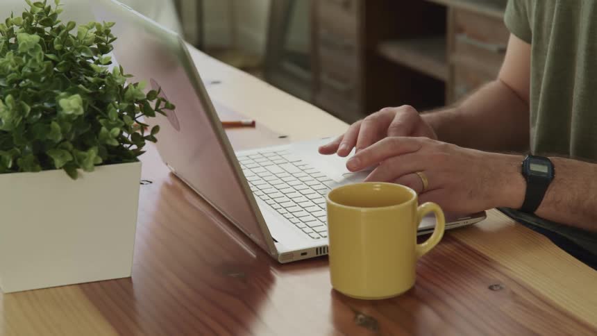 A male caucasian sitting at a table typing on a laptop