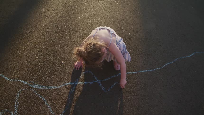 A young girl kneels to draw on the street with blue chalk