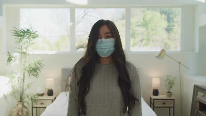 A teenage girl standing in a bedroom with a mask on