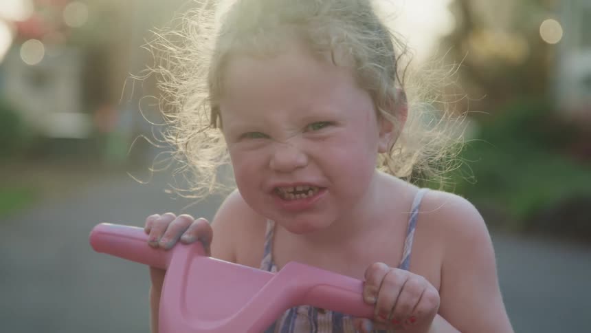 Close up of a little girl on a tricycle mugs the camera at sunset