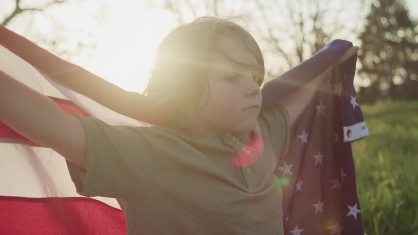A little boy outside holding an american flag behind his back
