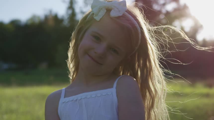Little blonde girl with a white dress smiles warmly and faces the camera with eye contact