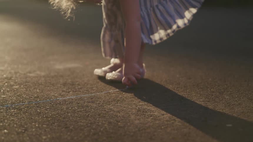 A little girl draws on the cement with sidewalk chalk
