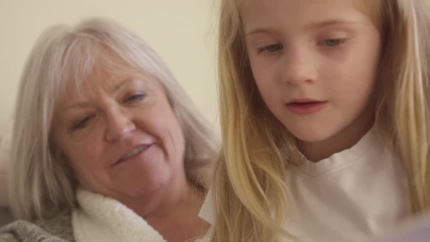 A little girl looks at something out of frame while sitting on her smiling grandmothers lap