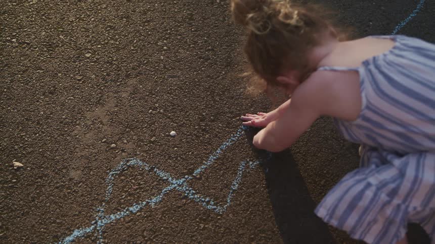 A little girl drawing on the cement with sidewalk chalk