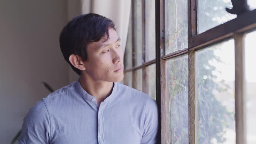 Asian man with a blue shirt looks out the window