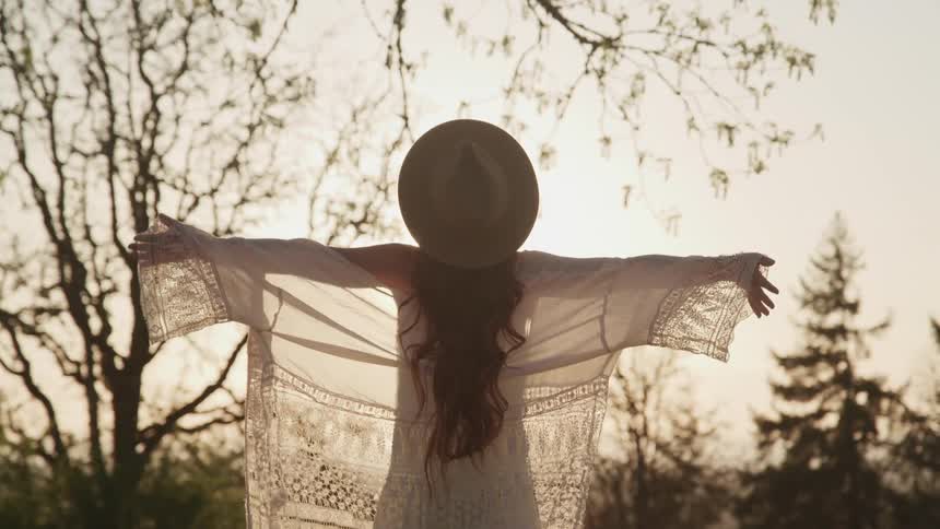 A woman wearing a sunhat stretches her arms towards the sky