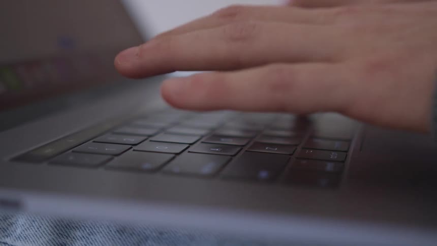 Close up of a persons hands typing on a space grey laptop