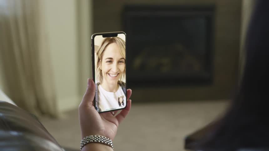 A woman sits in her living room and chats with a friend on her smartphone