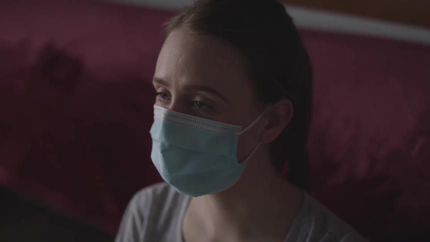 Woman with a ponytail and a light blue mask looks into space