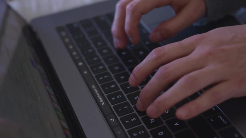 Close up of a persons hands typing on space grey laptop