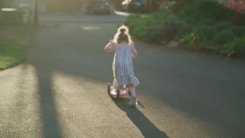 A child is riding a scooter down the driveway