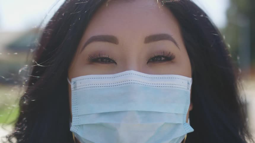 Asian woman with straight black hair and a light blue mask faces the camera with eye contact