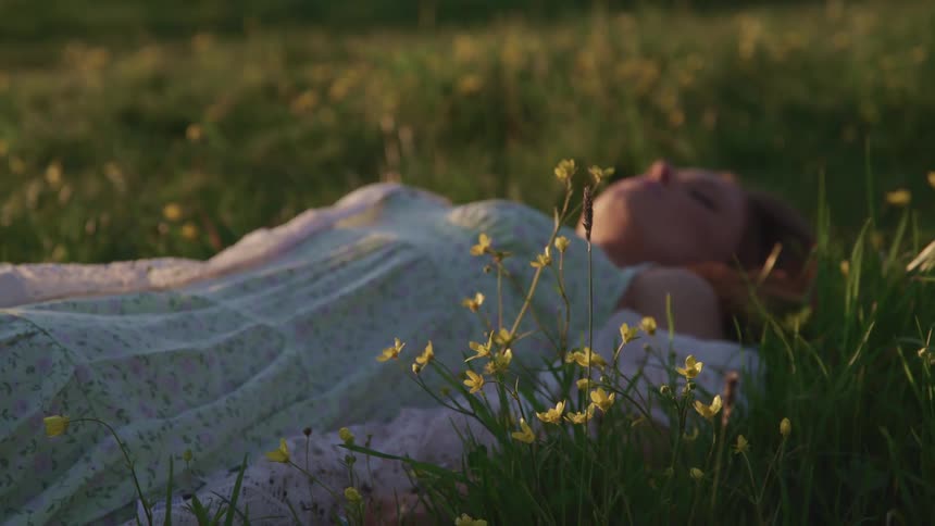 Woman wearing a dress lays on her back over the grass in a prairie