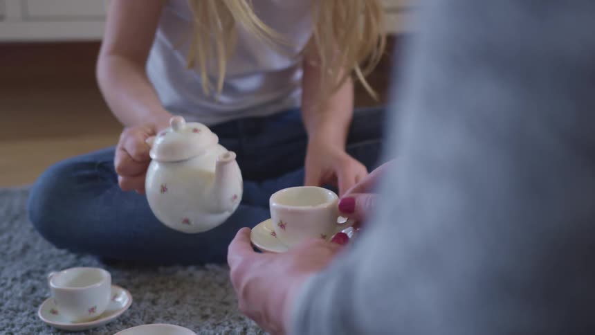 A girl has a tea party with her mother at home