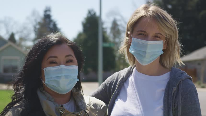 Couple of friends wearing blue face masks stand in front of the houses on a neighborhood