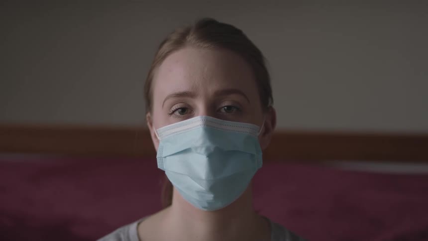 Woman with a ponytail and a blue mask faces the camera with eye contact
