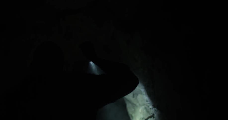 A person holding a flashlight walks through a dark cave