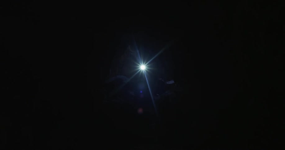 A person holding a flashlight walks through a dark area