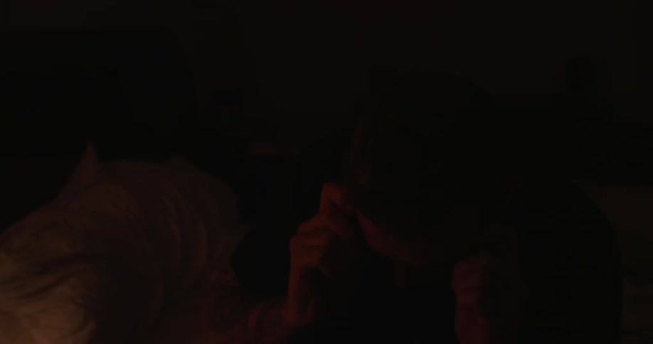 A man leans forward and puts his glasses on in a dark room