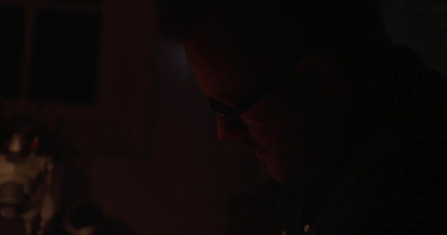 A man writes at a desk in a dark room