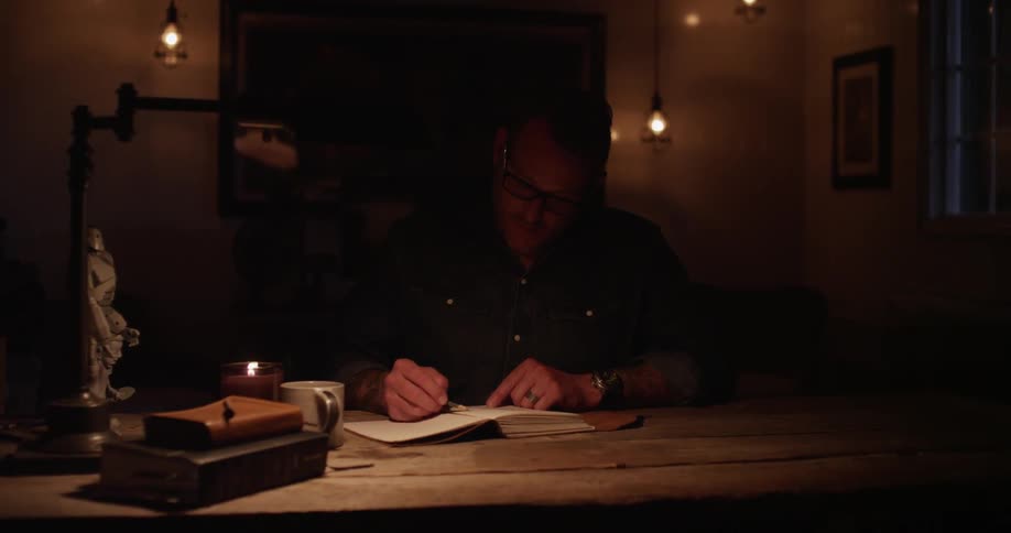 A man is writing in a notebook at a desk