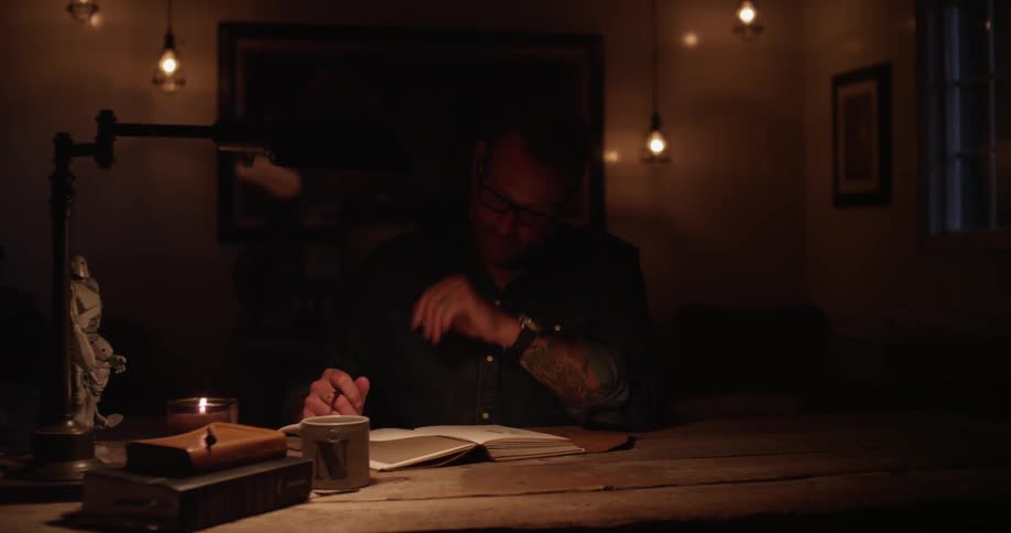 A man sits at a table with a notebook and is thinking and drawing