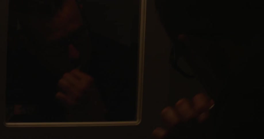 The reflection of a man brushing his teeth in a dimly lit bathroom