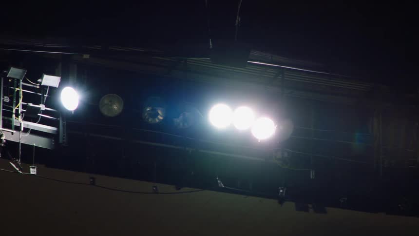 Several bright lights shine down from metal scaffolding located in a studio where filming can occur