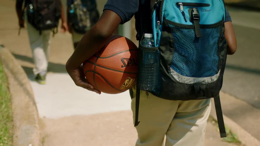 A boy in a school uniform carries a basketball as he follows behind two other boys