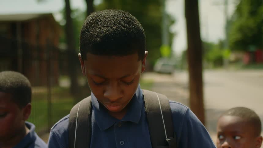 Young boys carrying backpacks and a basketball walk on the neighborhood street