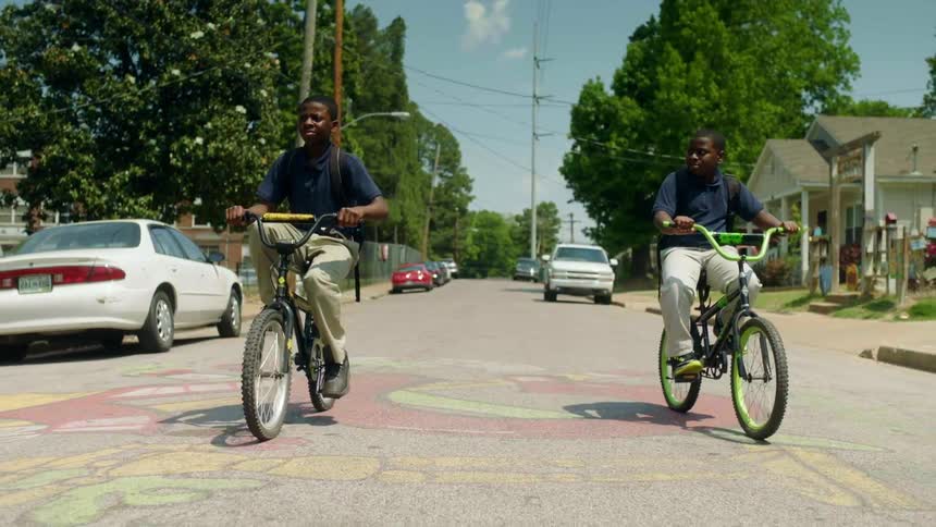 Two boys riding bikes down a neighborhood street