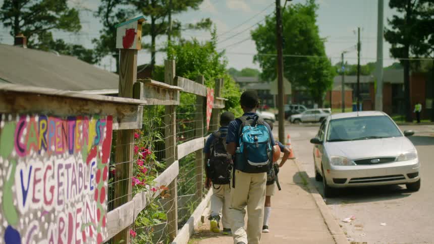 Three boys in school uniforms walking along a sidewalk while one of them dribbles a basketball
