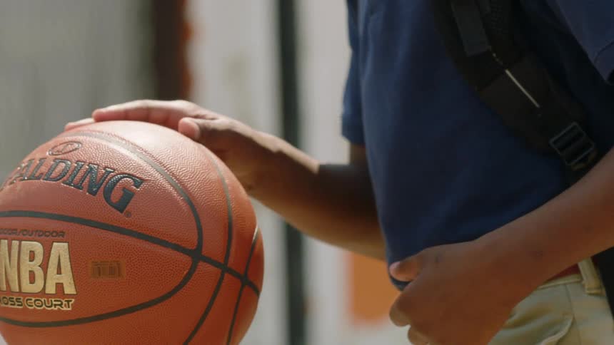 Kid wearing a backpack dribbles a basketball outdoors