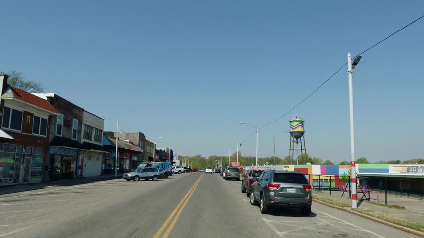Carsoccupy side of road near empty sidewalks and parking lots near storefronts