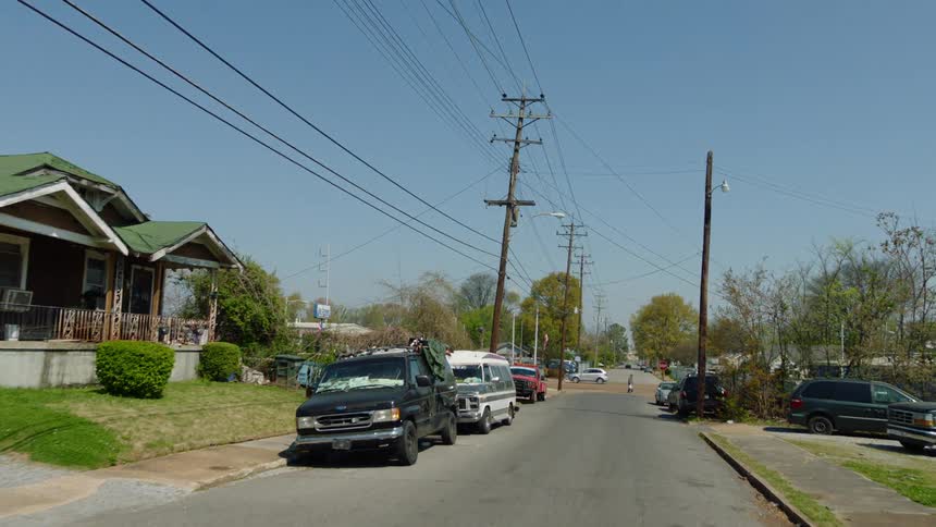 A pedestrian crossing a street in a neighborhood with cars lining the road