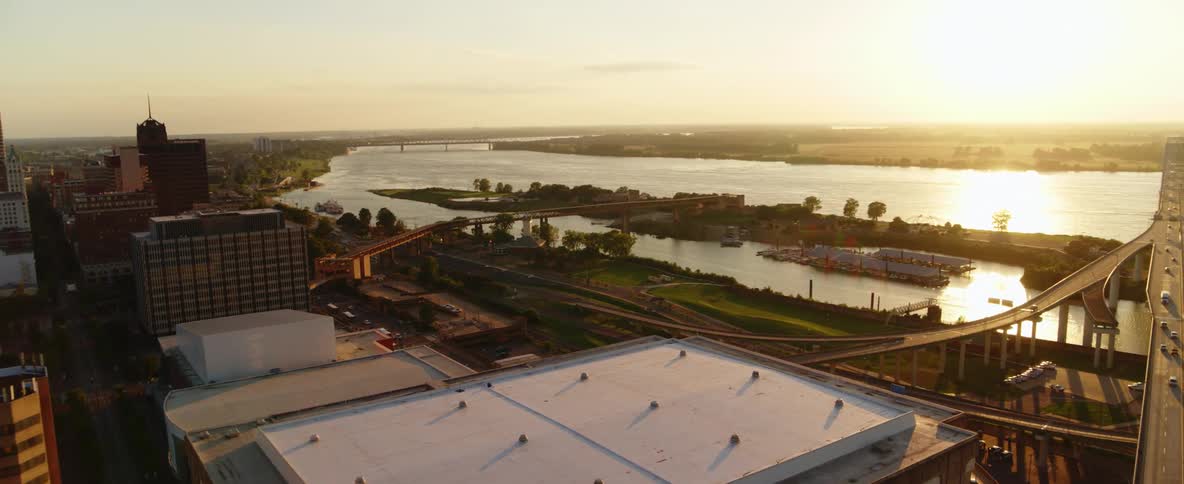 River reflects suns glare paralleling large highway running past building of city downtown near pyramid shaped building