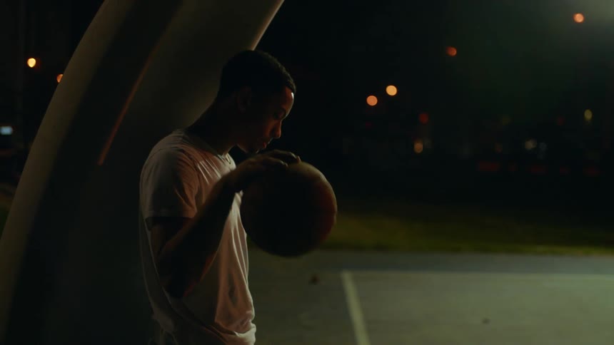 Young man dribbles a basketball standing alone in a basketball court at night