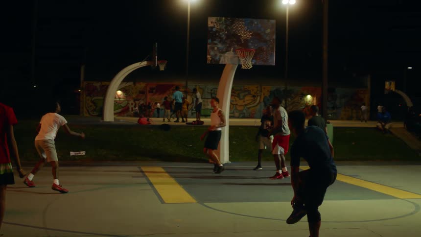A group of young men play basketball at a public court at night