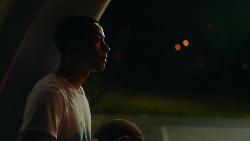 A black male dribbling a basketball outside in the dark