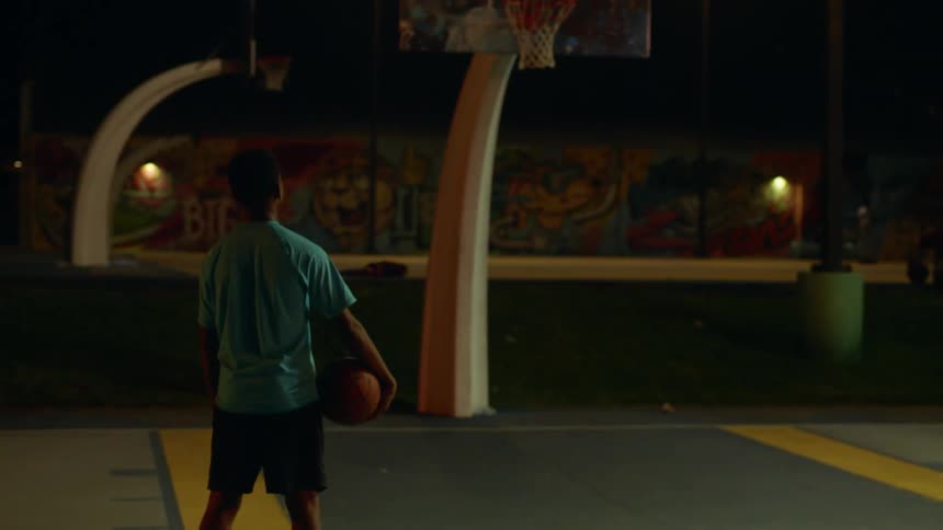 A teenage boy holding a basketball stares at the hoop