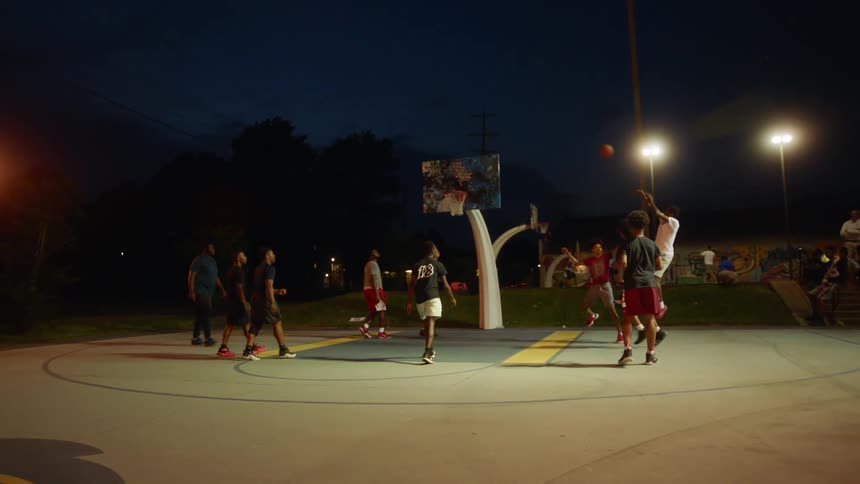 A group of black males playing basketball on a basketball court at night
