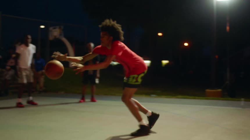 Men play basketball on court at night under park lights