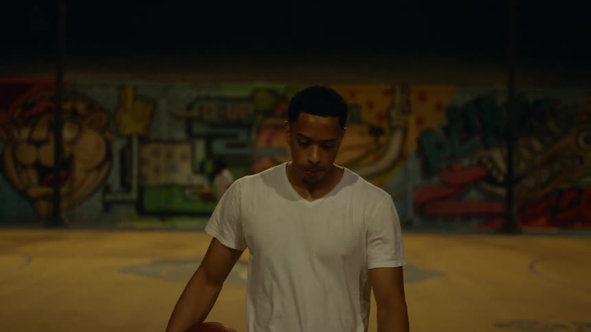 Young man carries a basketball on a court under stadium lights at night