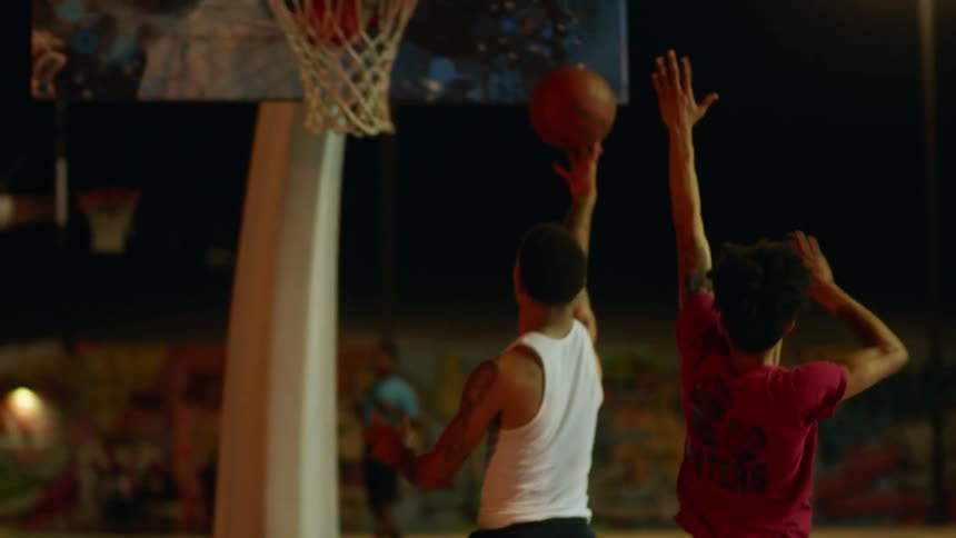 Spectators watch men play basketball at night on park basketball court