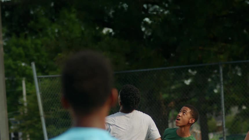 Group of teenagers play basketball in an outdoors court at day