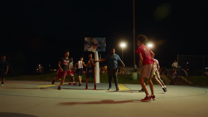 Young black men play basketball on an outdoor basketball court at night