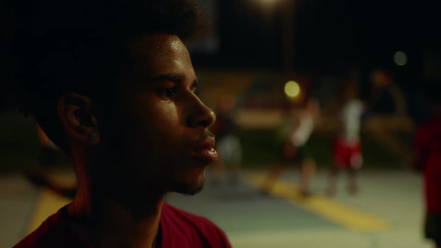 Men play basketball on court in park at night