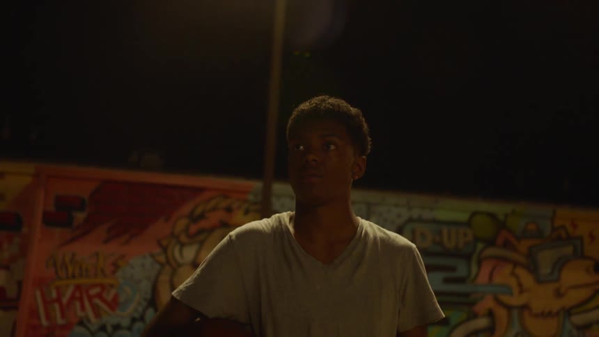 A young man carrying a basketball walks under street light at night